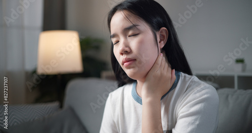 Portrait of Unwell young woman has neck pain while sitting on the sofa in the living room. People with muscle-body problems