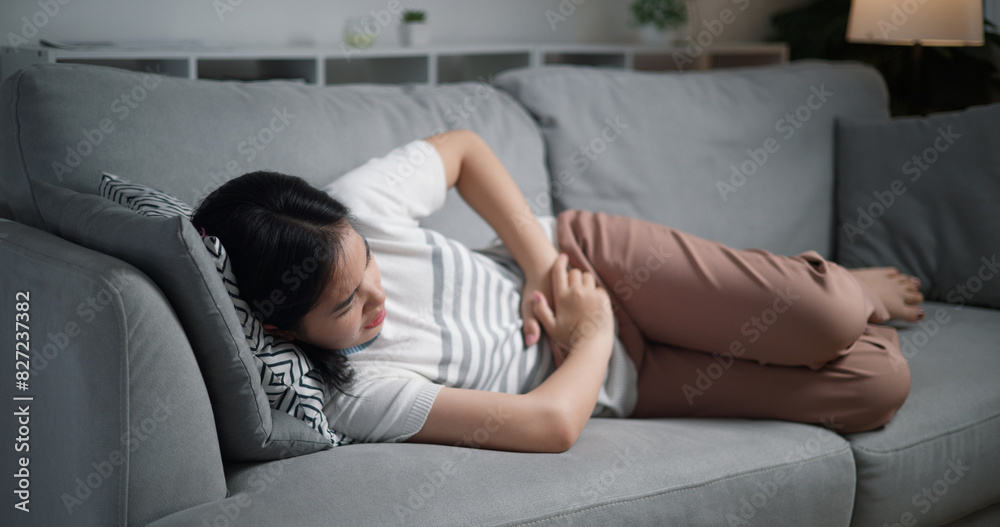 Portrait of Unwell young woman suffering from severe stomach ache while lying on sofa in the living room, feeling extremely sick, female experiencing period cramps. Portrait of Unwell young woman suffering from severe stomach ache while lying on sofa in the living room, feeling extremely sick, female experiencing period cramps.