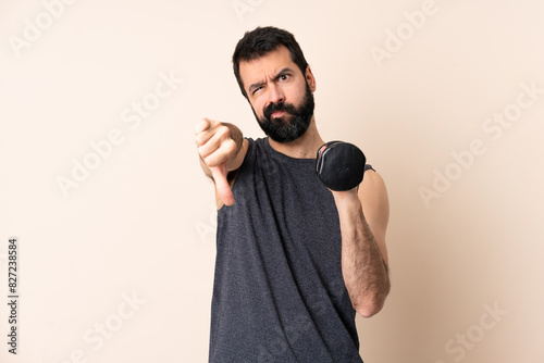 Caucasian sport man with beard making weightlifting over isolated background showing thumb down with two hands
