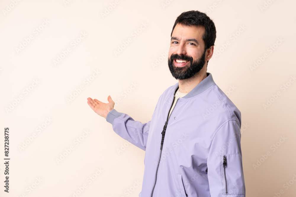 Caucasian man with beard wearing a jacket over isolated background extending hands to the side for inviting to come Caucasian man with beard wearing a jacket over isolated background extending hands to the side for inviting to come