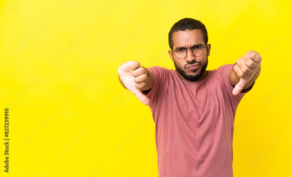 Young latin man isolated on yellow background showing thumb down with two hands Young latin man isolated on yellow background showing thumb down with two hands