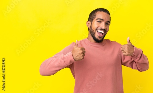 Young latin man isolated on yellow background giving a thumbs up gesture