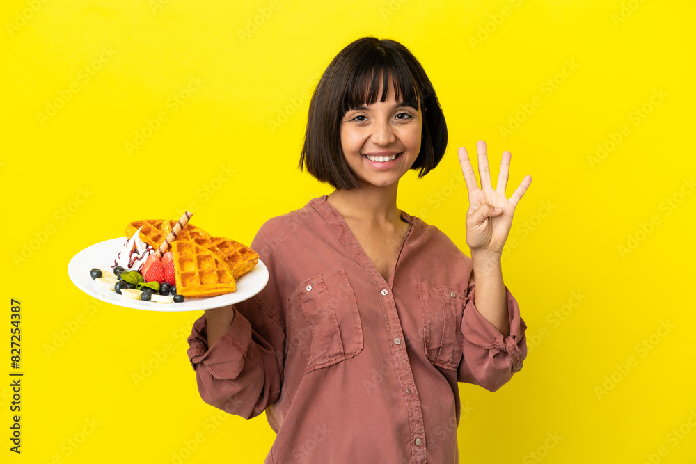 Pregnant woman holding waffles isolated on yellow background happy and counting four with fingers Pregnant woman holding waffles isolated on yellow background happy and counting four with fingers