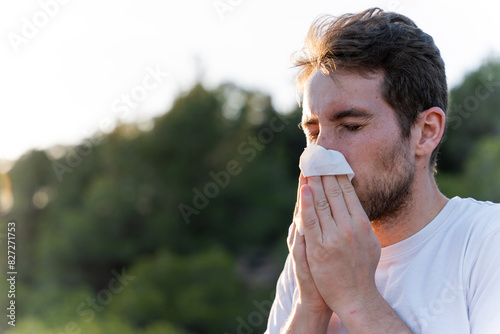 Fotografía Sick man surrounded by nature blowing his nose and sneezing for pollen allergy s