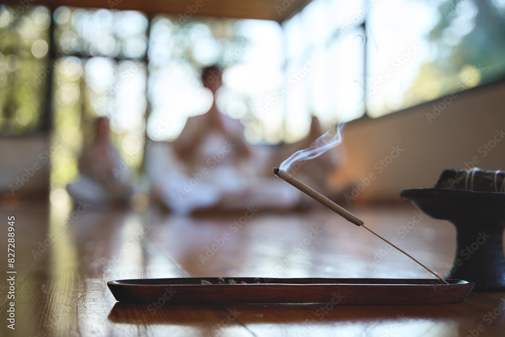 Scented stick on a wooden stand holder. Burning aromatic incense smoky stick with meditating people group doing yoga on background. Aromatherapy smoke for yoga and meditation healing practices concept