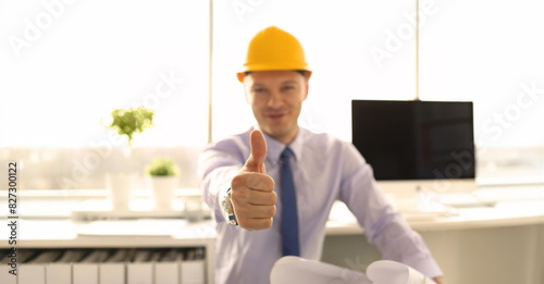 Creative Achitect Working at Engineering Office. Smiling Designer in Yellow Helmet at Workplace Showing Thumb Up Sign Shallow Focus. Project Engineer Approve Project Looking at Camera photo