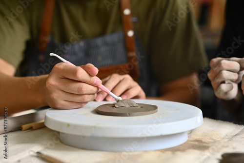 Close-up of an artist's hands sculpting clay on a pottery wheel, using a sculpting tool, showcasing precision and artistry in a creative studio setting