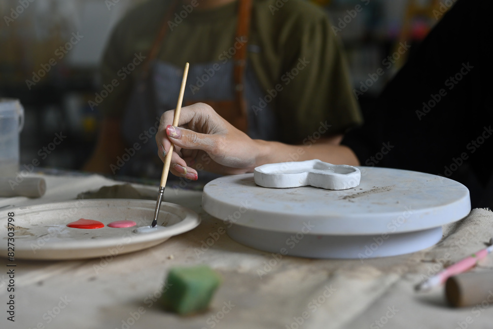 A close-up of an artist's hand holding a brush and mixing paints on a palette. A heart-shaped ceramic piece is being painted on a rotating platform A close-up of an artist's hand holding a brush and mixing paints on a palette. A heart-shaped ceramic piece is being painted on a rotating platform