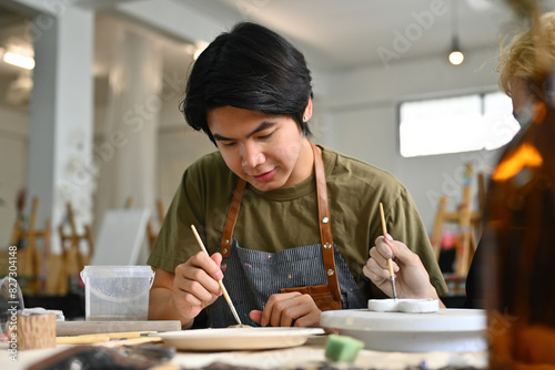 Two teenage Asian students focused on painting ceramic pieces in an art classroom together
