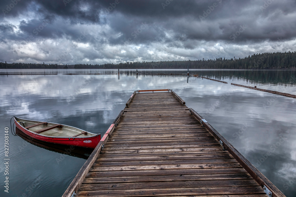 Naklejka premium a wooden dock next to a lake under cloudy skies with a red boat