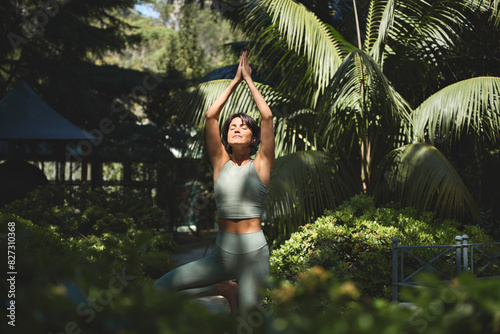 Принти на полотні Fit sporty mindful young Hispanic woman meditating doing yoga breathing exercises with eyes closed feeling peace of mind, mental balance standing in green nature tropical park on sunny day