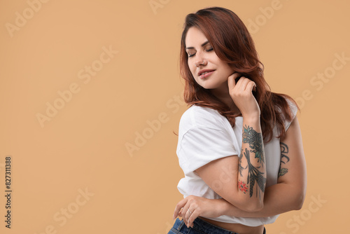 Beautiful tattooed woman on beige background, space for text