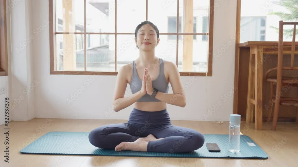 Asian woman in workout attire practices meditation on a yoga mat in her home's sitting room. Perfect for showcasing relaxation and mindfulness in a domestic setting Asian woman in workout attire practices meditation on a yoga mat in her home's sitting room. Perfect for showcasing relaxation and mindfulness in a domestic setting
