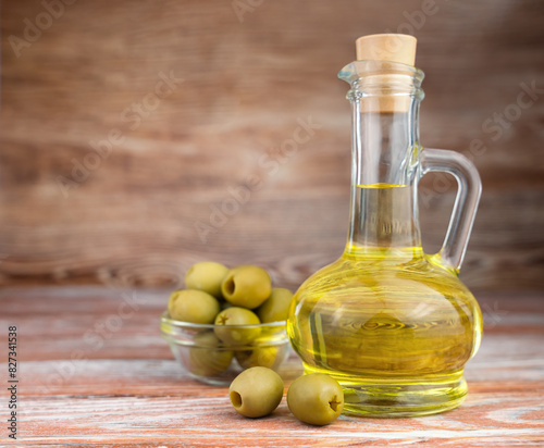 Bottle of fresh extra virgin olive oil and green olives on wooden background. Close-up. Copy space.