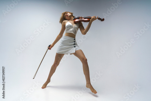 young blonde female musician plays the violin moving on one leg