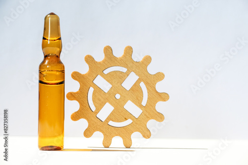 Cosmetic ampoule and wooden gear on a beige background. Hair growth trigger concept.