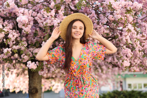 Beautiful woman in straw hat near blossoming tree on spring day