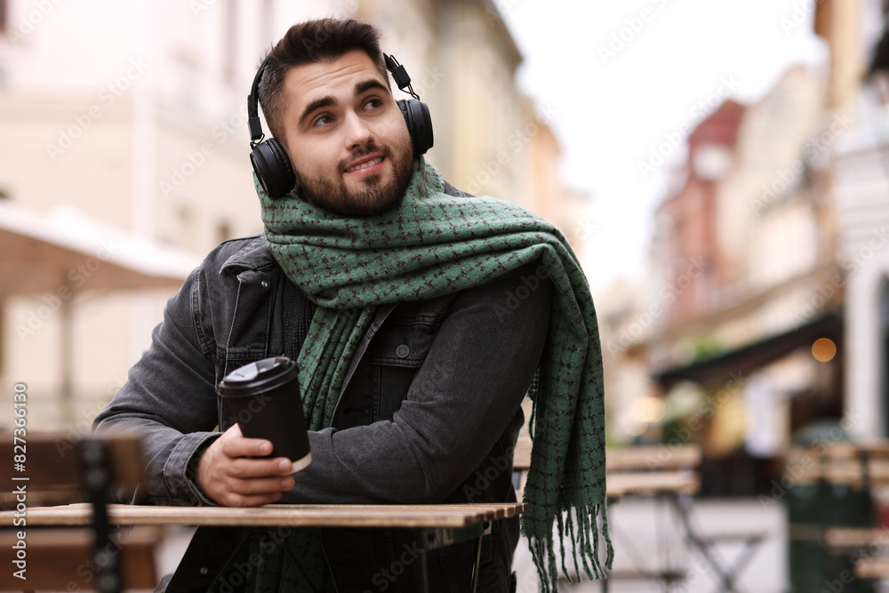 Smiling man in warm scarf with paper cup listening to music in outdoor cafe Smiling man in warm scarf with paper cup listening to music in outdoor cafe