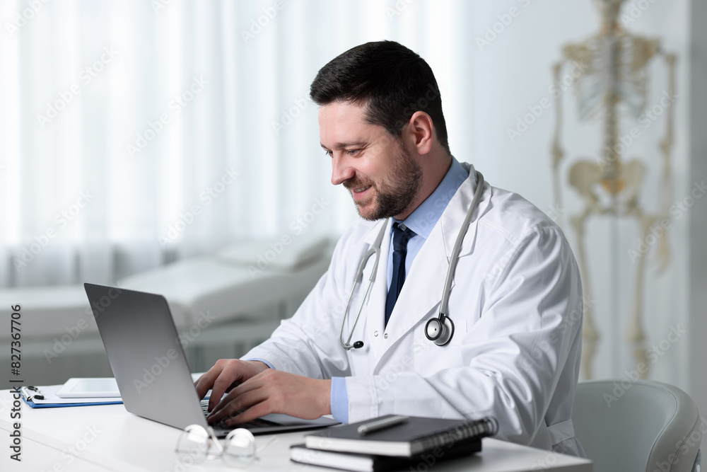 Smiling doctor having online consultation via laptop at table in clinic Smiling doctor having online consultation via laptop at table in clinic