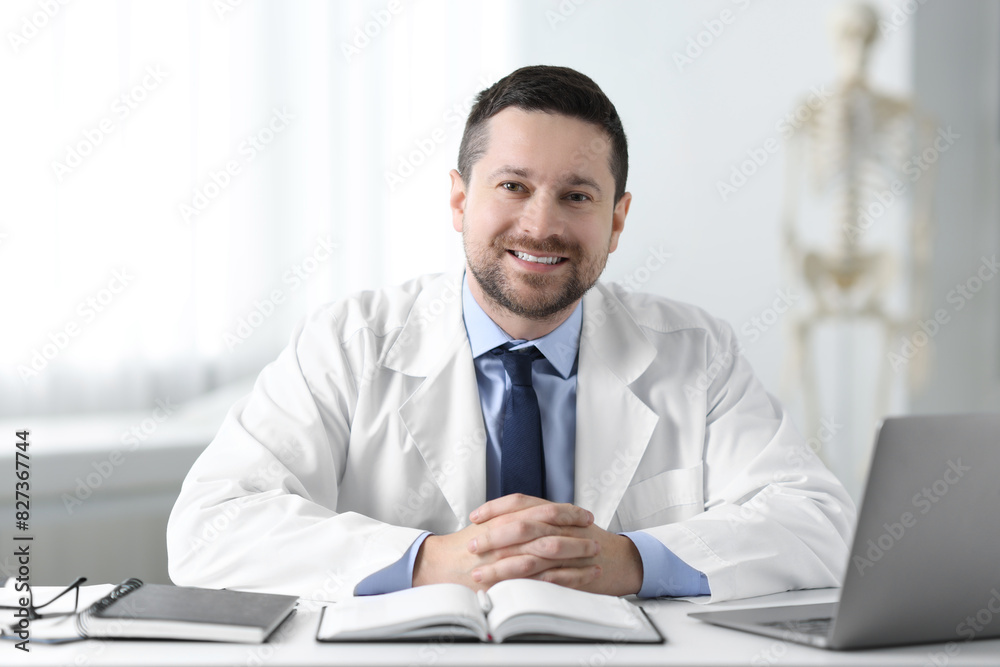 Smiling doctor with laptop at table in clinic. Online medicine Smiling doctor with laptop at table in clinic. Online medicine