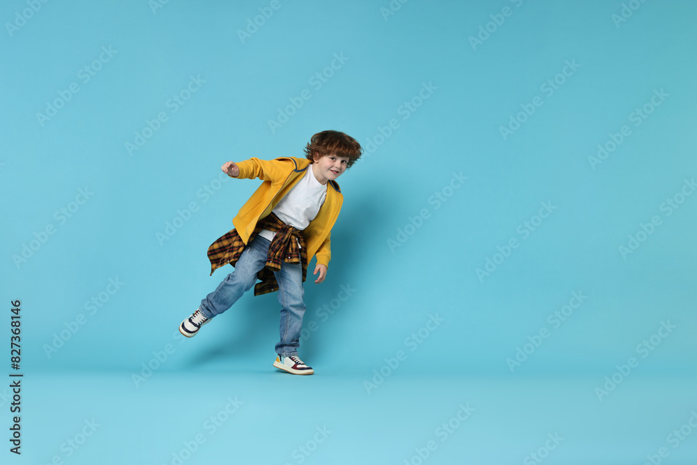 Happy little boy dancing on light blue background. Space for text