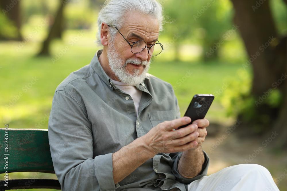 Portrait of happy grandpa with glasses using smartphone on bench in park
