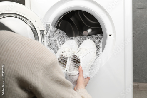 Woman putting stylish sneakers into washing machine, closeup