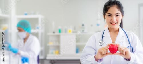 Smile beautiful young Asian doctor hold heart shape in hand standing at laboratory background 