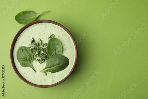 Delicious spinach cream soup with fresh leaves and microgreens in bowl on green background, top view. Space for text