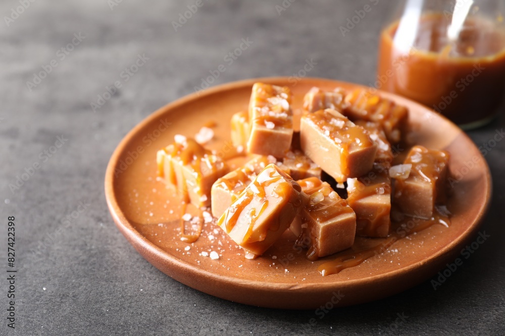 Plate with tasty candies, caramel sauce and salt on grey table, closeup Plate with tasty candies, caramel sauce and salt on grey table, closeup