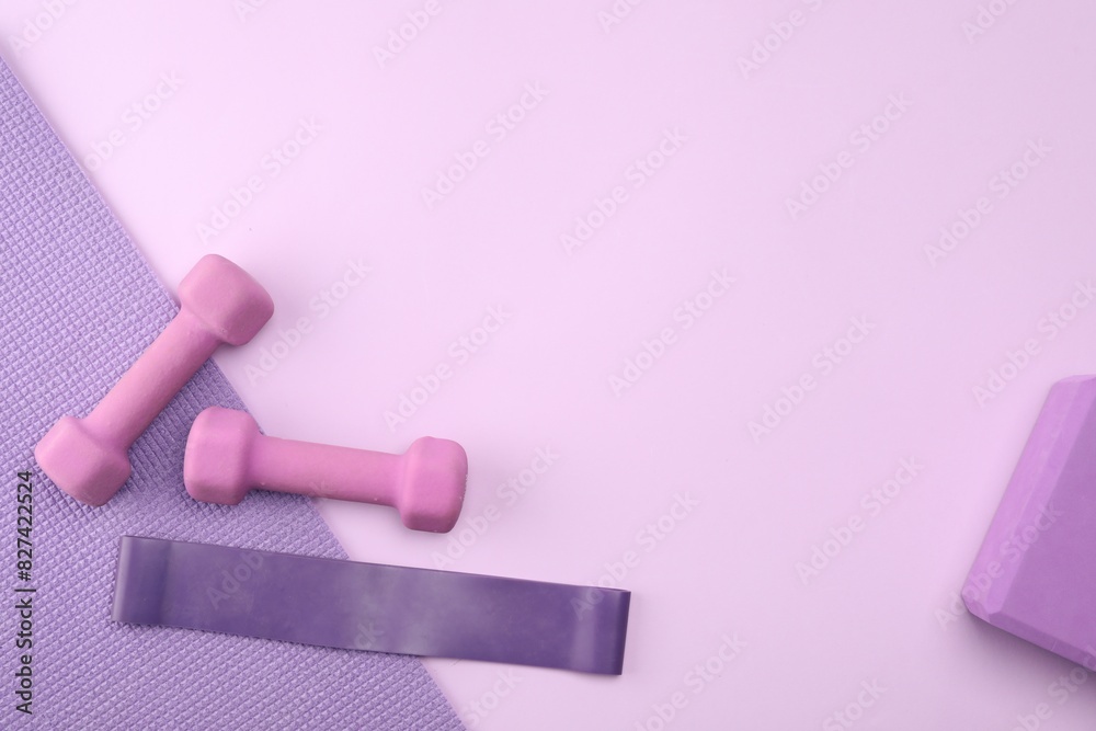 Two dumbbells, yoga block, mat and fitness elastic band on violet background, flat lay. Space for text Two dumbbells, yoga block, mat and fitness elastic band on violet background, flat lay. Space for text