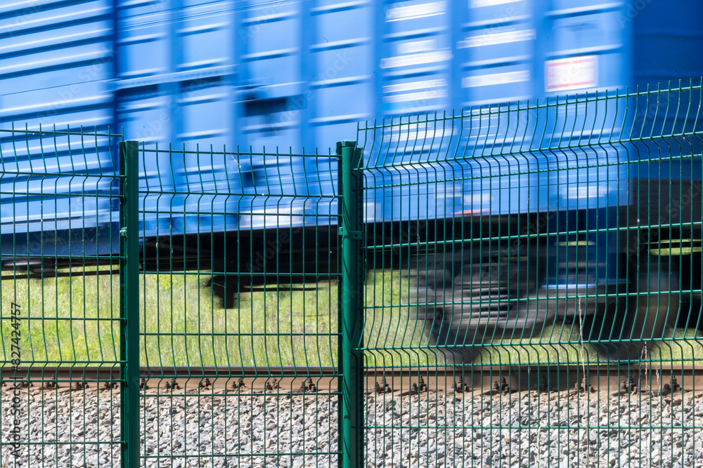 Obraz premium A metal fence behind which a train passes. Railroad fencing. Ensuring the safety of railway transport. Steel fence