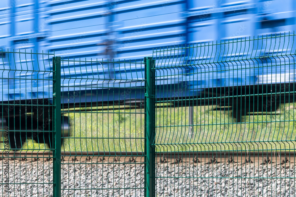 Obraz premium A metal fence behind which a train passes. Railroad fencing. Ensuring the safety of railway transport. Steel fence