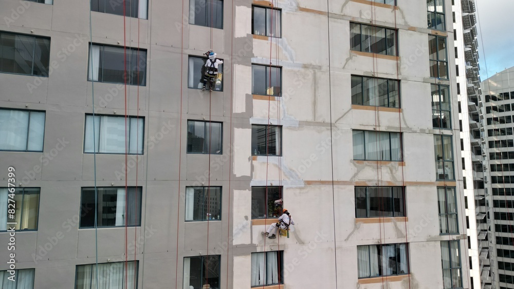 This captivating drone photo shows skilled workers performing maintenance tasks on a scaffold at a considerable height. The precision and risk involved in urban repair are evident in their actions. This captivating drone photo shows skilled workers performing maintenance tasks on a scaffold at a considerable height. The precision and risk involved in urban repair are evident in their actions.