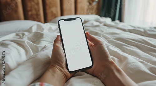 Close-up of a Hand Holding an iPhone with a Blank Screen on White Bed Sheets, Perfect for App Mockups and Digital Presentations, Clean and Minimalistic Background © Vanessa
