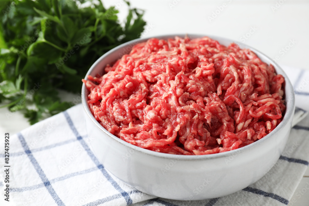 Raw ground meat in bowl and parsley on table, closeup Raw ground meat in bowl and parsley on table, closeup