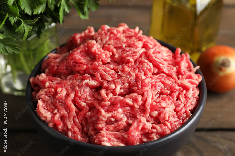 Raw ground meat in bowl and parsley on wooden table, closeup