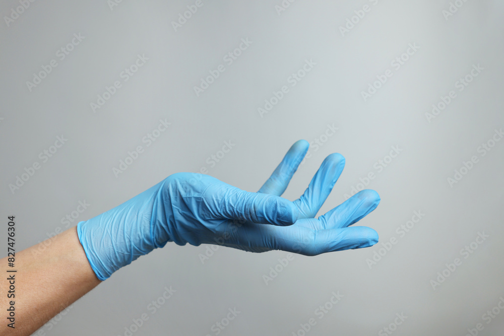 Doctor wearing light blue medical glove holding something on grey background, closeup