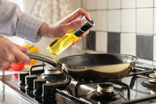 Vegetable fats. Woman sprinkling oil into frying pan on stove in kitchen, closeup photo