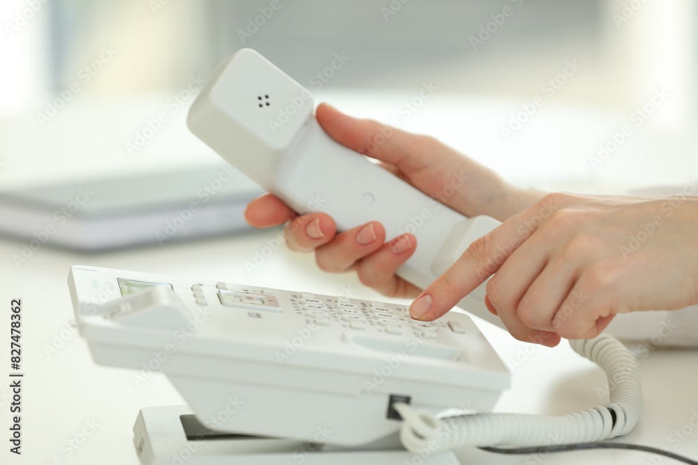 Assistant dialing number on telephone at white table, closeup