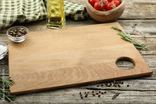 Cutting board, rosemary, oil and pepper on wooden table. Space for text