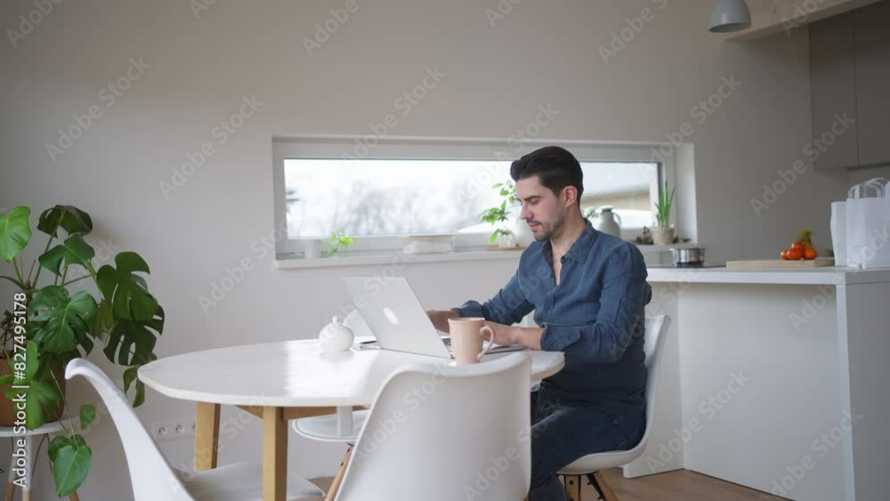 Man working from home office, using laptop, sitting at kitchen table with cup of hot coffee. Working remotely from living room. Man working from home office, using laptop, sitting at kitchen table with cup of hot coffee. Working remotely from living room.