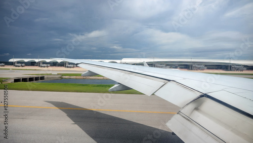 Through the airplane window, Suvarnabhumi International Airport comes into view, along with the expansive wings of the aircraft, amid the midday hustle.