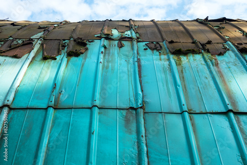 A fragment of the side surface of an old semicircular hangar made of green metal sheets. Remnants of roofing material are visible on the roof. Background.