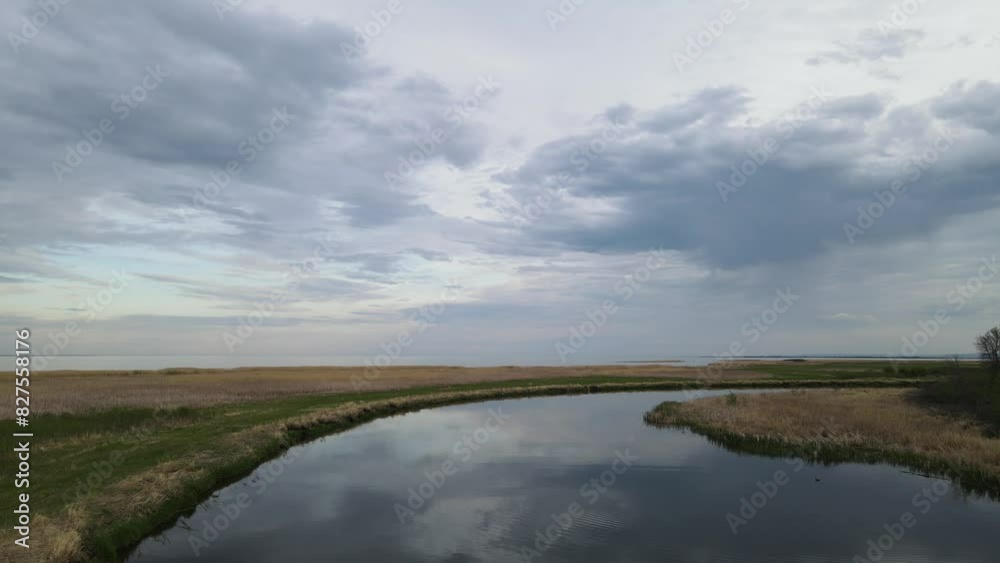Drone flying forward low over a calm winding river that is reflecting a sky full of light to dark gray clouds. The river is surrounded with dry and green grass.
Drone flying forward low over a calm winding river that is reflecting a sky full of light to dark gray clouds. The river is surrounded with dry and green grass.