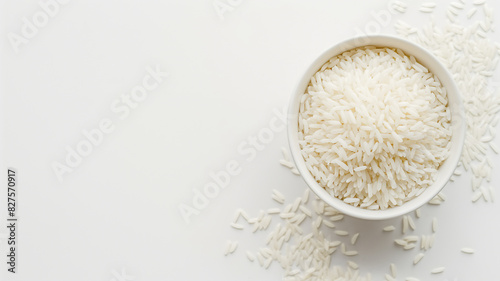 A white bowl filled with uncooked white rice grains, some scattered around on a clean white surface.