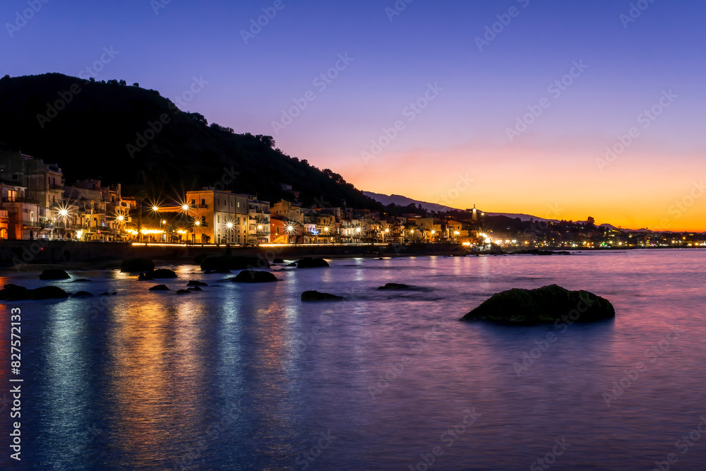 evening or night landscape of evening town coastline in golden lights and sea gulf with calm water and nice reflections with beautisul sunset sky on background