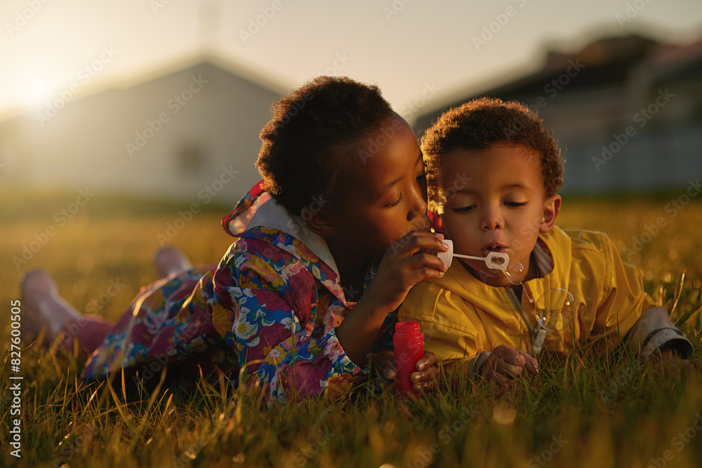 Nature, sunset and children blowing bubbles in park relaxing on grass together for bonding. Family, fun and kid siblings playing with soap toy laying on lawn in outdoor garden or field in evening. Nature, sunset and children blowing bubbles in park relaxing on grass together for bonding. Family, fun and kid siblings playing with soap toy laying on lawn in outdoor garden or field in evening.