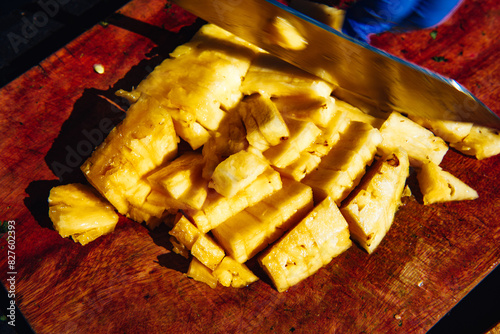 A knife cutting through slices of fresh pineapple on a wooden cutting surface, motion blur