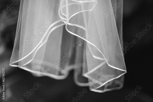 A black and white photo of the sheer bottom of a wedding dress hanging in a dark closet photo